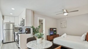 Een compacte hotelkamer met kitchenette, een bed, een eethoek en een televisie waarop streamingdiensten worden getoond.