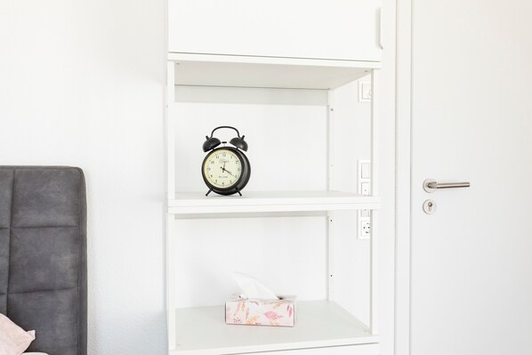 Une étagère blanche avec un réveil noir et une boîte de mouchoirs.