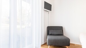 Una habitació amb un sofà gris, un televisor fixat a la paret i cortines translúcides.