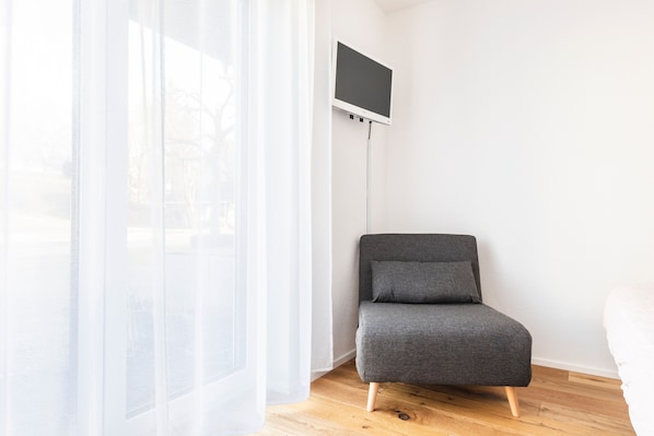 A room with a grey sofa, a TV mounted on the wall, and sheer curtains. - Studio "LandZeit" with Terrace & Wi-Fi (Neukirch)