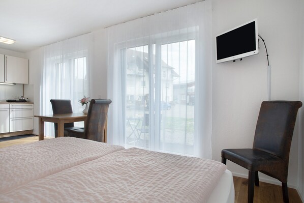 A hotel room with a bed, a desk, a chair, a TV, and large windows. - Holiday Apartment "LandZeit" with Terrace and Wi-Fi (Neukirch)