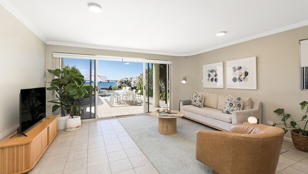 A modern living room with a TV, sofa, and coffee table, leading to a balcony with a view of the sea and a bridge. - Waterfront King Bed Courtyard Apartment (Sylvania)