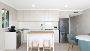 A modern kitchen with white cabinets, a stainless steel refrigerator, a dishwasher, and a wooden island with stools. - Waterfront King Bed Courtyard Apartment (Sylvania)