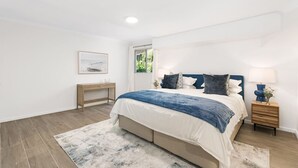 A bedroom with a bed, bedside tables, a nightstand, a framed picture on the wall, and a window. - Waterfront King Bed Courtyard Apartment (Sylvania)