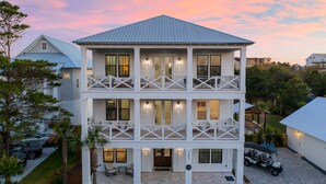 A two-story building with a balcony on each floor, a covered front porch, and a driveway with a golf cart. - The Belvedere - Luxury Vacation Rental Near the Beach with Huge Pool & Volleyball Court (Santa Rosa Beach)