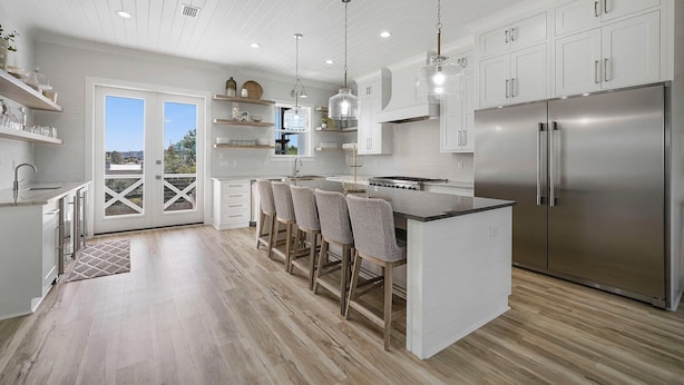 A modern kitchen with white cabinetry, a stainless steel refrigerator, and a central island with bar stools. - The Belvedere - Luxury Vacation Rental Near the Beach with Huge Pool & Volleyball Court (Santa Rosa Beach)