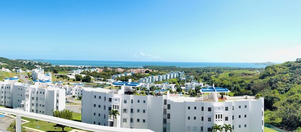 A coastal residential area with modern white buildings, a clear view of the sea, and lush greenery.