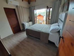 A bedroom with a bed, a wooden door, and a window with curtains.