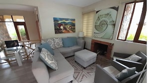 A living room with a sofa, ottoman, and armchairs, a fireplace, and a painting on the wall.