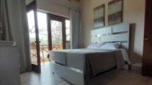 A bedroom with a bed, a desk, and a view through a glass door.