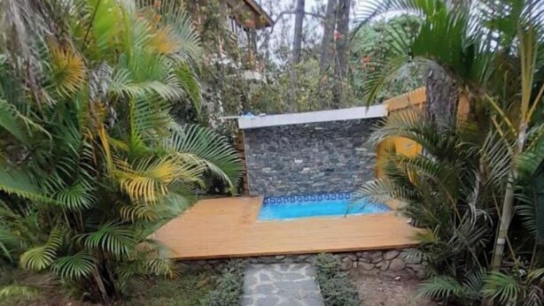 A stone pathway leading to a pool area surrounded by lush greenery and a stone wall.