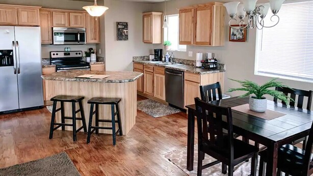 Une cuisine moderne avec des meubles en bois, un plan de travail en granit, un réfrigérateur en acier inoxydable et un coin repas comprenant une table et des chaises en bois.