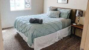 Une chambre à coucher avec un lit, une table de chevet, une lampe, une fenêtre et un tableau accroché au mur.