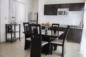 Uma cozinha moderna com armários escuros, uma mesa de jantar com cadeiras, uma máquina de café e um micro-ondas.