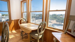 A dining area with a wooden table and chairs, large windows with a view of a residential neighborhood.