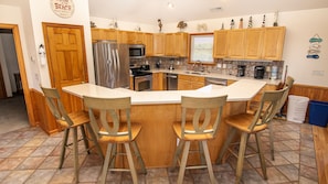Cocina con armarios de madera, refrigerador de acero inoxidable, horno doble, pileta y barra con taburetes.
