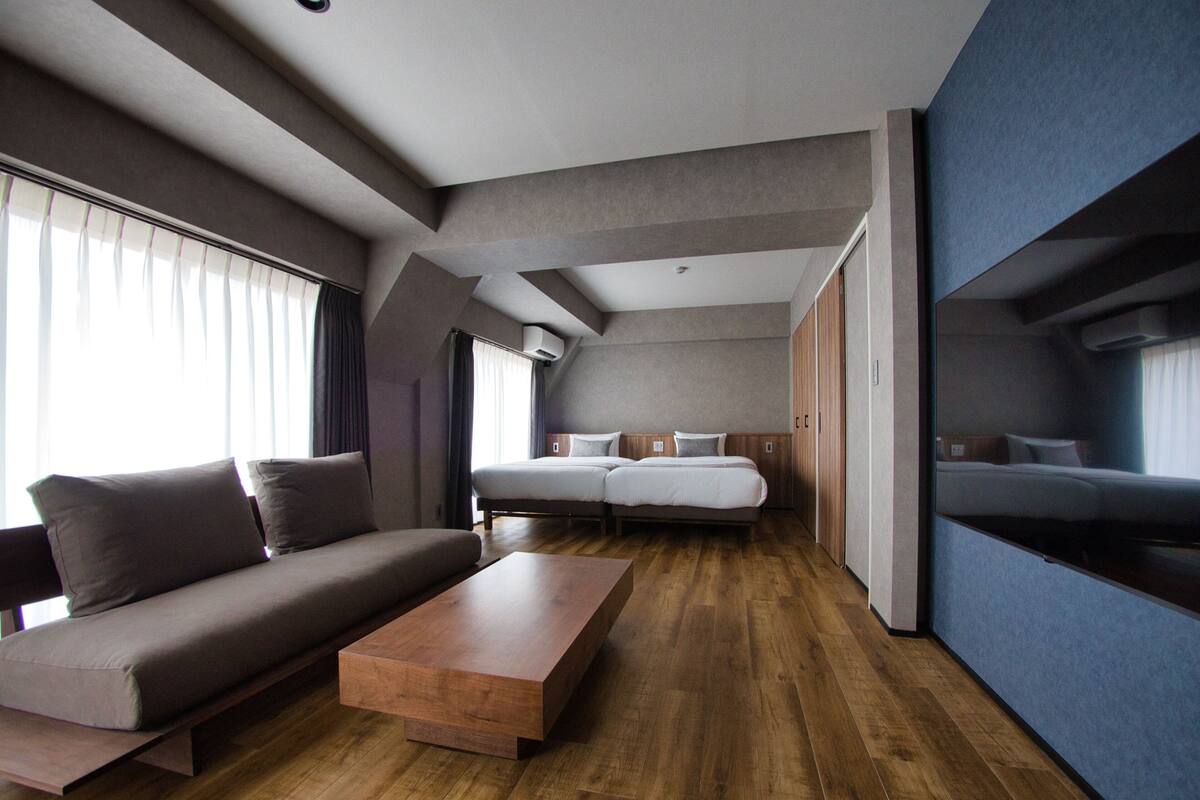 A modern hotel room with a sofa, a wooden coffee table, a double bed, and a wardrobe.
