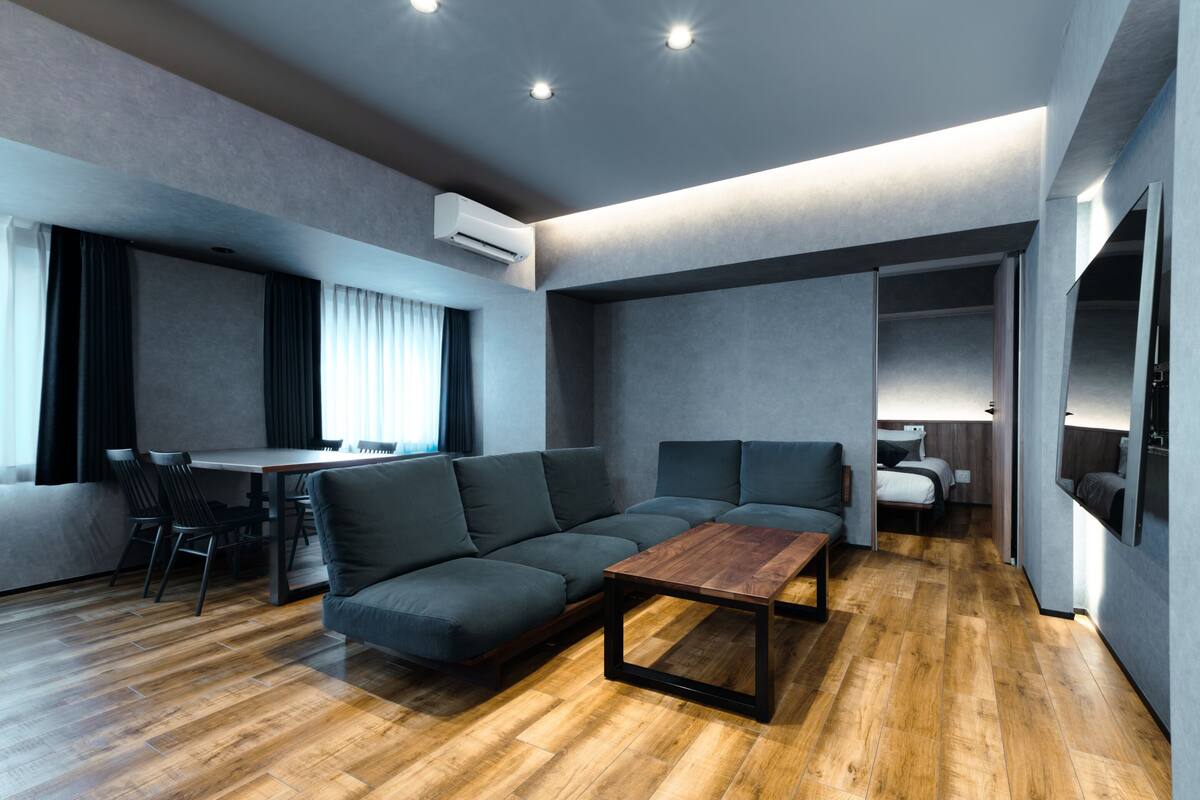 A modern living room with a sofa, a wooden coffee table, a dining area with chairs, and a small kitchenette.