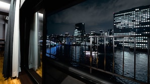 Una habitación con un ventanal grande que da a un paisaje urbano nocturno, mostrando un río y edificios iluminados.