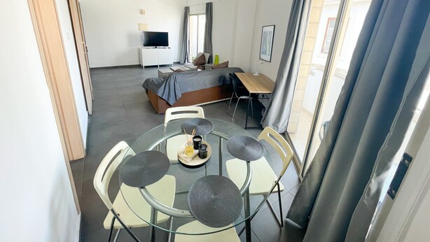 Una habitación de hotel moderna con cama, escritorio, televisor y un área de comedor con sillas y mesa.