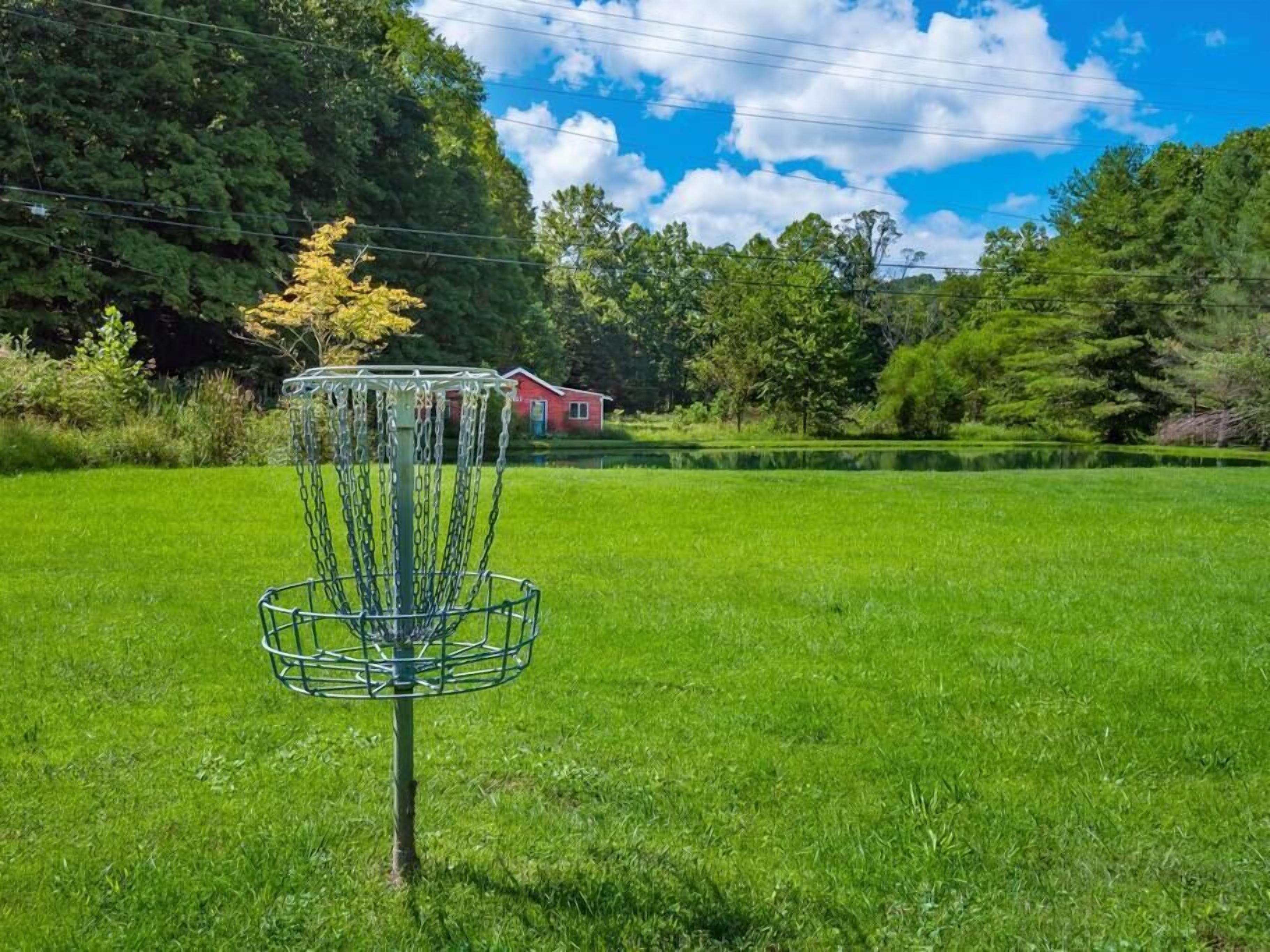 En discgolfkorg på en gräsklädd åker med en röd byggnad i bakgrunden.