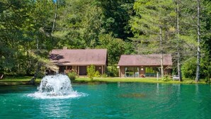 A cabin with a pond in front, surrounded by trees.