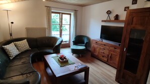 Una sala de estar con un sofá de cuero, una mesa de centro de madera, un sillón verde, un aparador de madera y un televisor.