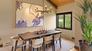 Ein Essbereich mit einem Holztisch, sechs Stühlen, einer Chandelüster, einem großen abstrakten Gemälde und einem Blumentopf.