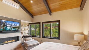 Ein Schlafzimmer mit Kamin, einem Bett, einem an der Wand befestigten Fernseher und großen Fenstern mit Blick auf die Berge.