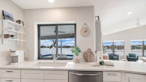A modern kitchen with a large window, a coffee machine, and a view of a body of water.