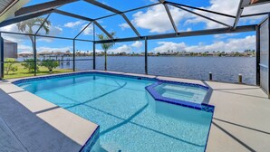 A swimming pool with a view of a lake, surrounded by a covered patio with a metal roof structure.
