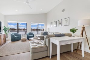 A modern living room with a sofa, two armchairs, a coffee table, a TV, and a large window with a view. - Luxury Gulf-Access Lakefront Retreat | Heated Pool, Spa, Bikes, Kayaks & Dock (Cape Coral)
