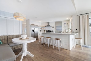 A modern kitchen with a central island, white cabinetry, and a dining area with a round table and bar stools. - Luxury Gulf-Access Lakefront Retreat | Heated Pool, Spa, Bikes, Kayaks & Dock (Cape Coral)