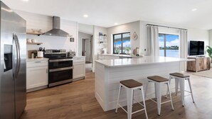 A modern kitchen with white cabinetry, stainless steel appliances, and a central island with stools.