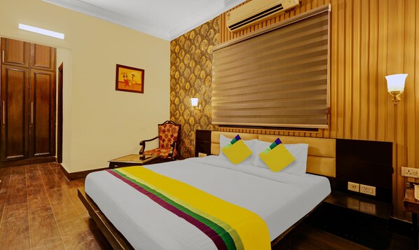 A hotel room with a bed, a chair, a wall-mounted air conditioner, and a door.