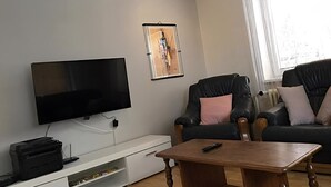 Un soggiorno con una TV a schermo piatto, due divani in pelle, un tavolino in legno e un'opera d'arte incorniciata appesa al muro.