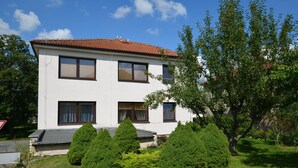 Un edificio bianco a due piani con tetto in tegole rosse, circondato da verde curato e alberi.