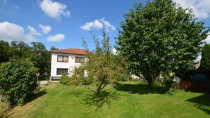 Una casa bianca con tetto rosso, circondata da un prato curato e alberi.