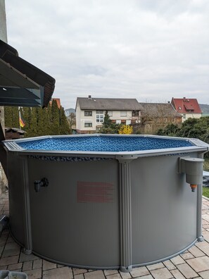 A large, grey above-ground pool with a blue interior, surrounded by a brick patio.