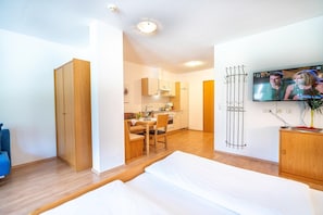 Een compacte kamer met een bed, een kleine kitchenette, een eethoek en een televisie.