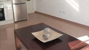 Une cuisine moderne avec des meubles blancs, un réfrigérateur en acier inoxydable, une table en bois foncé agrémentée d’un objet décoratif en verre, et un téléviseur à écran plat fixé au mur.