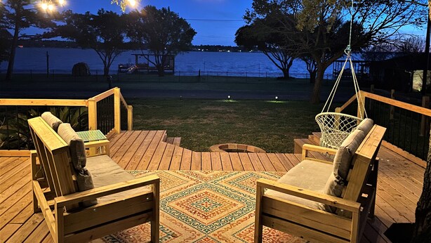 Una terraza de madera con mobiliario exterior, luces colgantes y vista al agua.