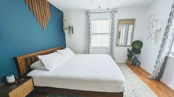 Un dormitorio con cama de madera, una mesita de noche, ventilador de techo, ventana con cortinas y un espejo fijado a la pared.
