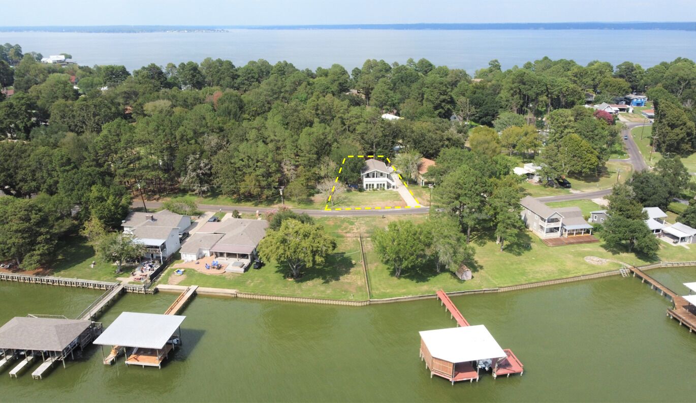 An aerial view of a lakeside property with a large house, docks, and surrounding greenery.