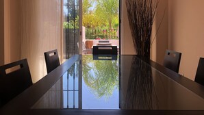 A modern dining area with a glass-top table, black chairs, and a view of a garden through a glass door.