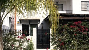 A white building with a black gate, steps leading to the entrance, and potted plants.