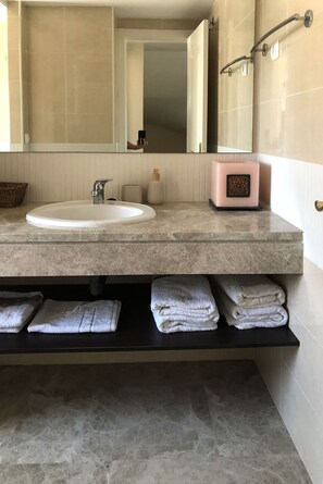 A bathroom with a marble sink, a mirror, a towel rack, and a shelf with folded towels.