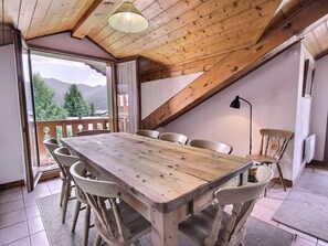 Ein Holzespeisetisch mit Stühlen in einem Raum mit schrägen Wänden und Blick auf Berge durch eine Glastür.