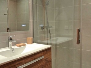 Un baño moderno con ducha de vidrio, lavamanos blanco y tocador de madera.