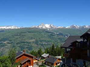 A mountain lodge with wooden architecture, a view of snow-capped mountains, and a valley below.